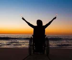 Handicapped woman in a wheelchair holding fire sparklers on the beach